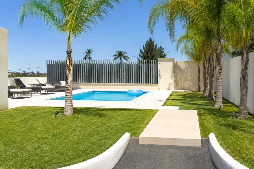 Piscina y zona recreativa exterior en Marbella Dog Club con césped natural, palmeras y área de relax para perros.